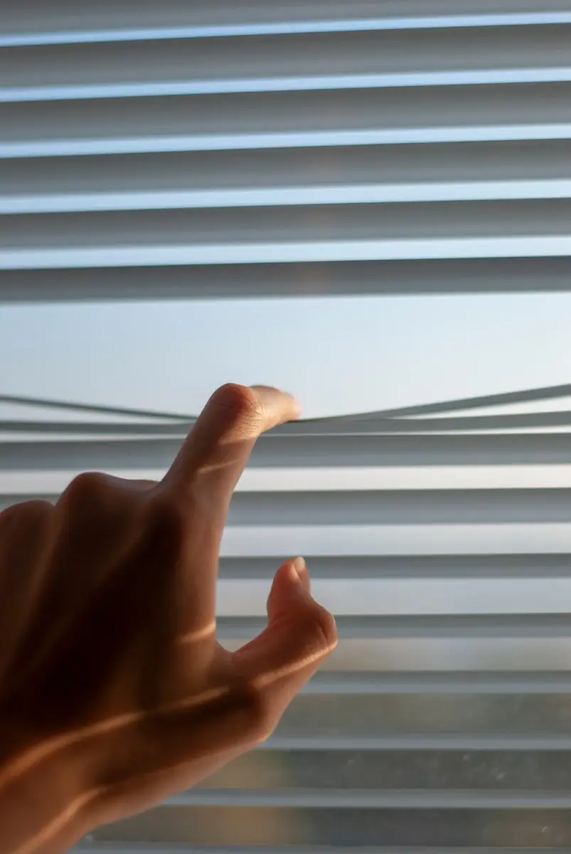 persons hand near white window blinds